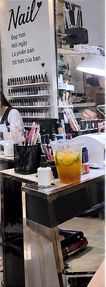 A narrow interior view shows nail-polish displays, manicure supplies and drinks arranged around a salon workstation.